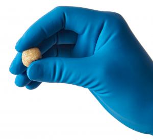 A blue-gloved hand holding a small rounded pellet of putty-like graft material.