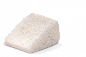 A wedge-shaped block of porous, sponge-textured white bone graft material.