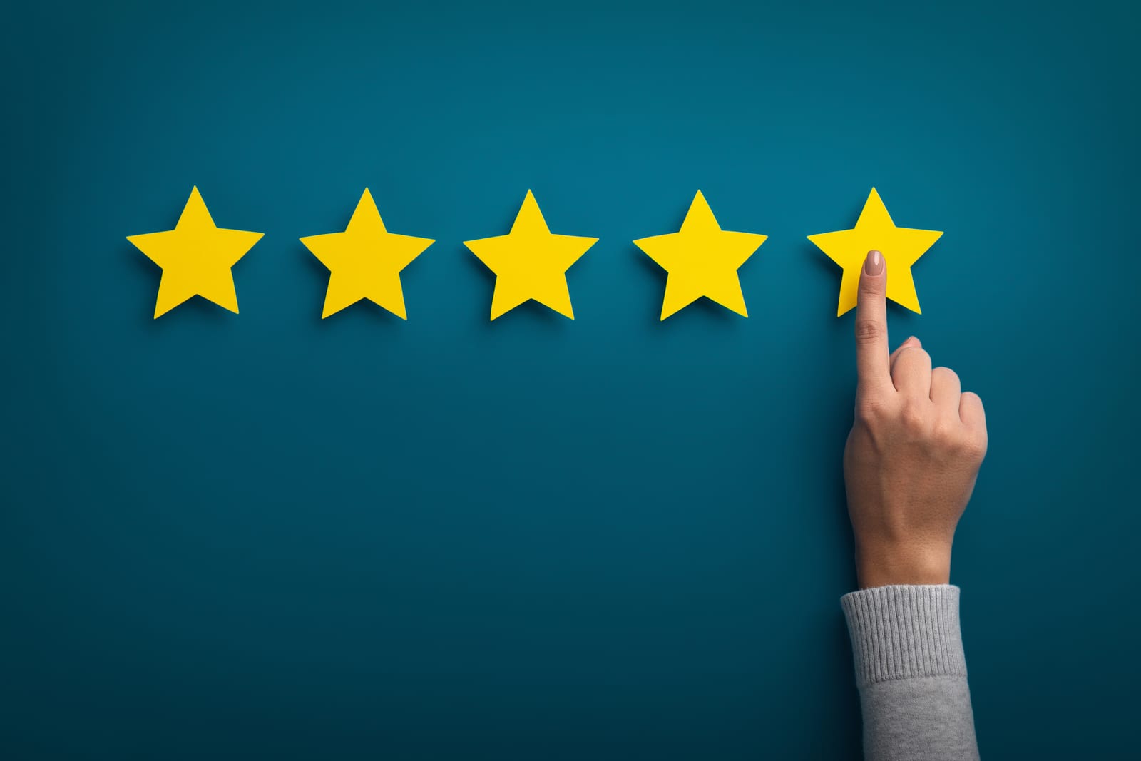 Close-up of a hand touching the fifth of five yellow stars against a teal background, symbolizing a five-star rating