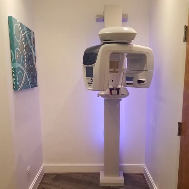 Floor-mounted CBCT scanner installed in a small alcove with decorative wall art and purple accent lighting