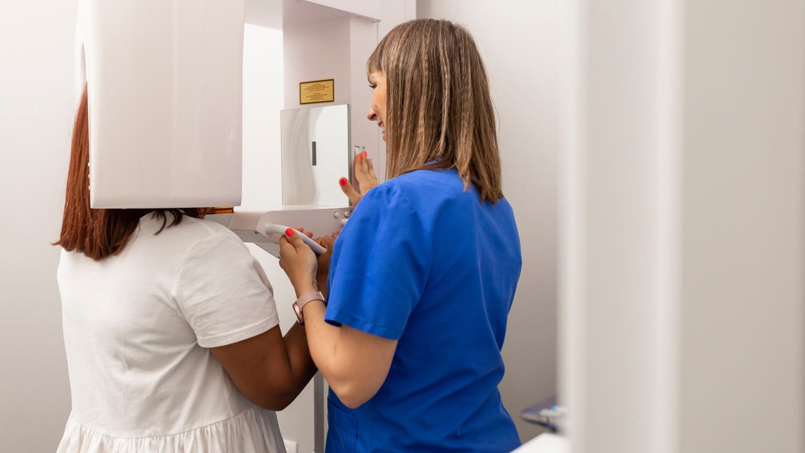 A dental staff member in blue scrubs positioning a patient's head inside a panoramic imaging unit